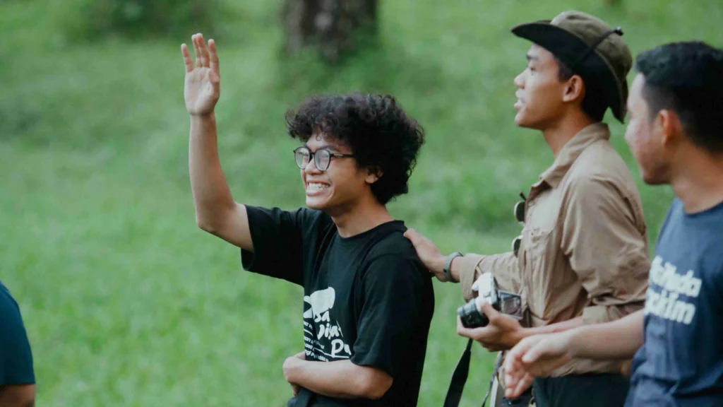 Sekelompok anak muda generasi Z sedang mengikuti aktivitas outdoor teamwork, berdiskusi sambil tersenyum, melatih soft skill leadership di alam terbuka